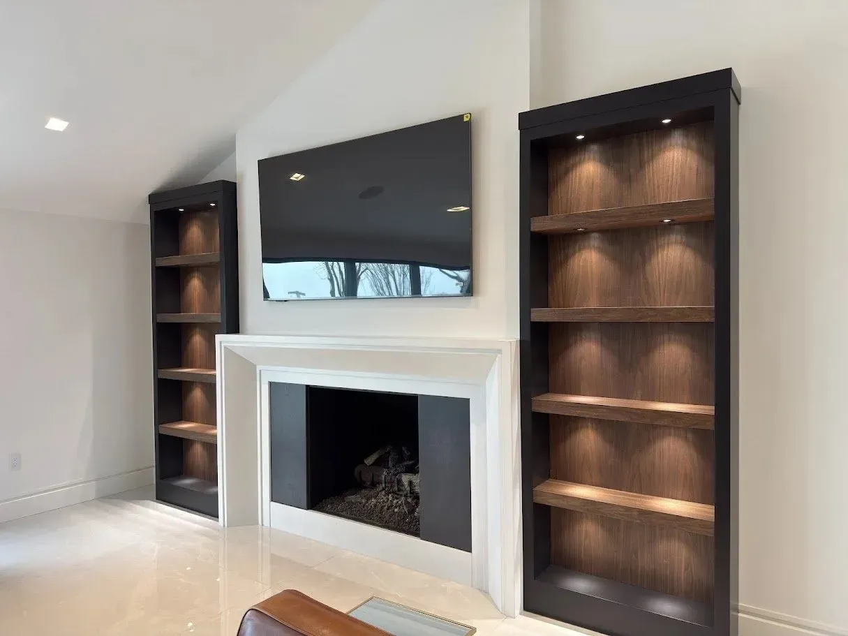 A white fireplace sits between two tall, dark wood built-in bookshelves with integrated lighting under a wall-mounted TV.