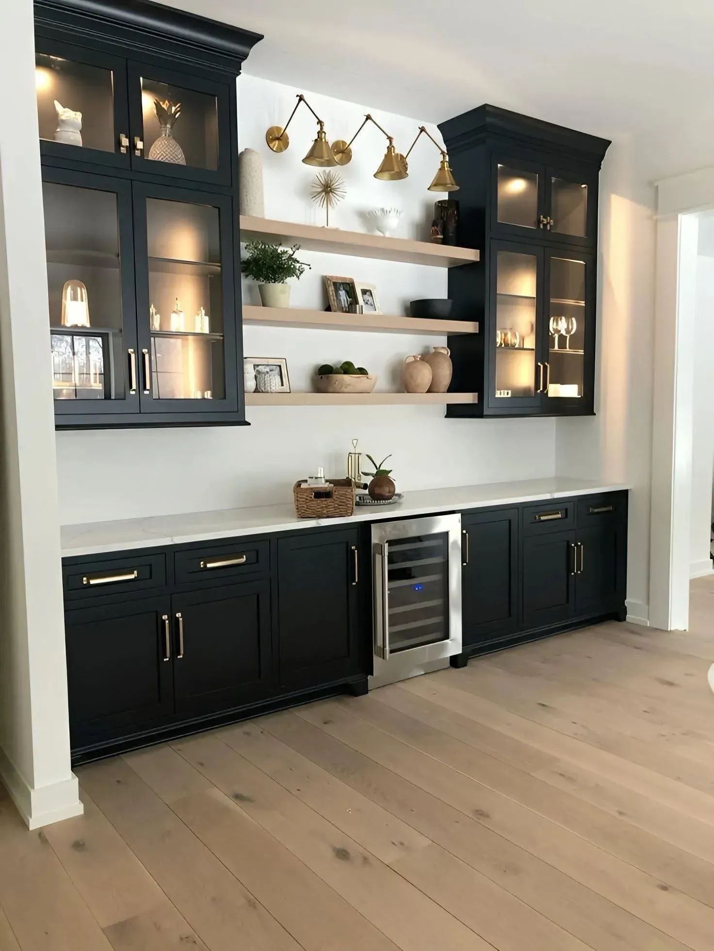 A dry bar with black cabinets, glass upper display cases with interior lighting, open wood shelving, and a wine cooler.