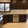 Modern kitchen featuring dark wood cabinets, a stainless steel dishwasher, a granite countertop, and light-colored flooring.