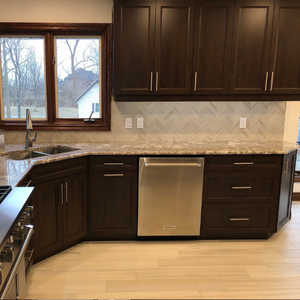 Modern kitchen featuring dark wood cabinets, a stainless steel dishwasher, a granite countertop, and light-colored flooring.