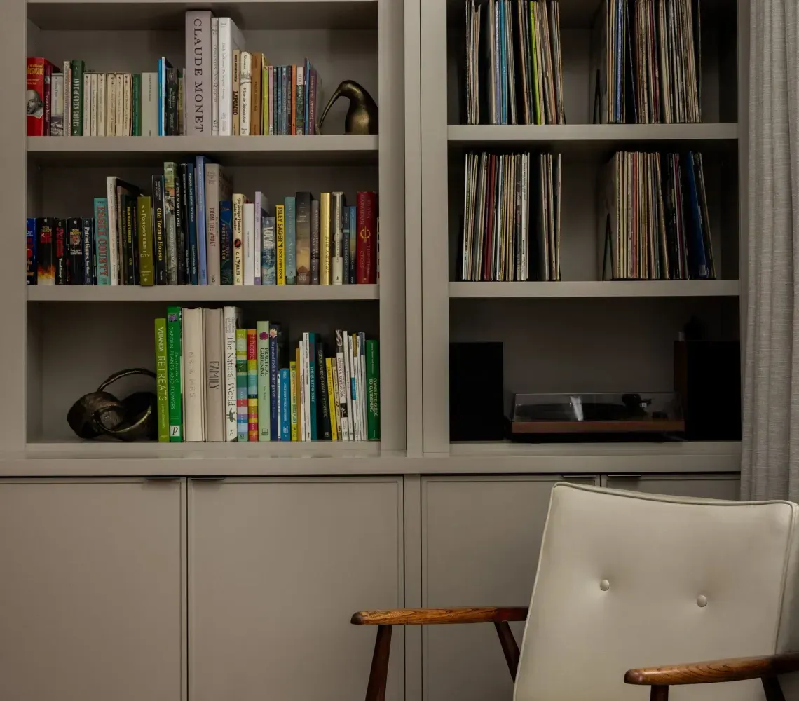 A cream-colored upholstered armchair sits next to floor-to-ceiling bookshelves filled with books and vinyl records.