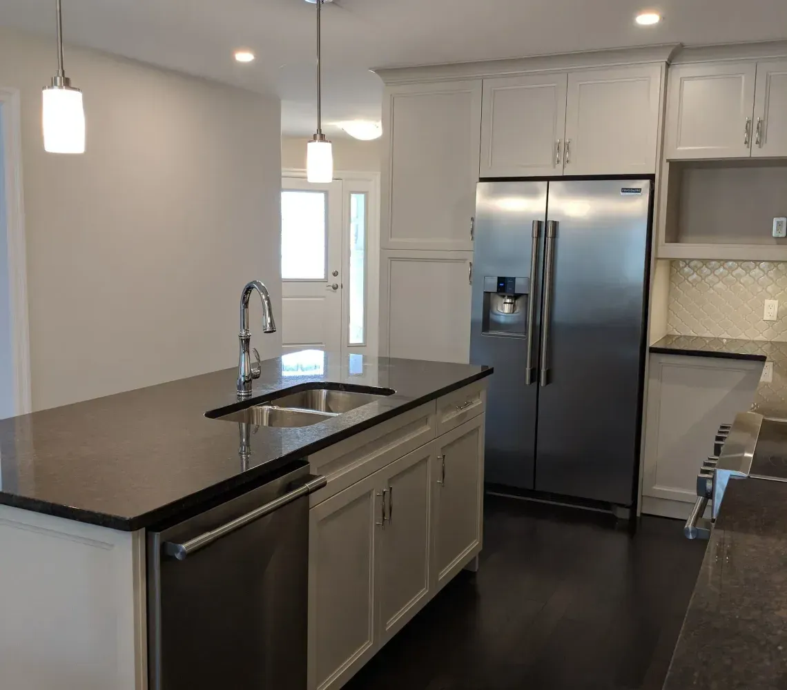 A kitchen island with a sink and dishwasher sits before a stainless-steel refrigerator and white cabinets.