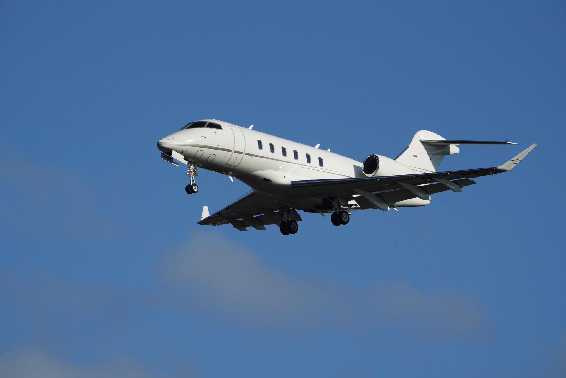 White private jet flying against a clear blue sky, landing gear down
