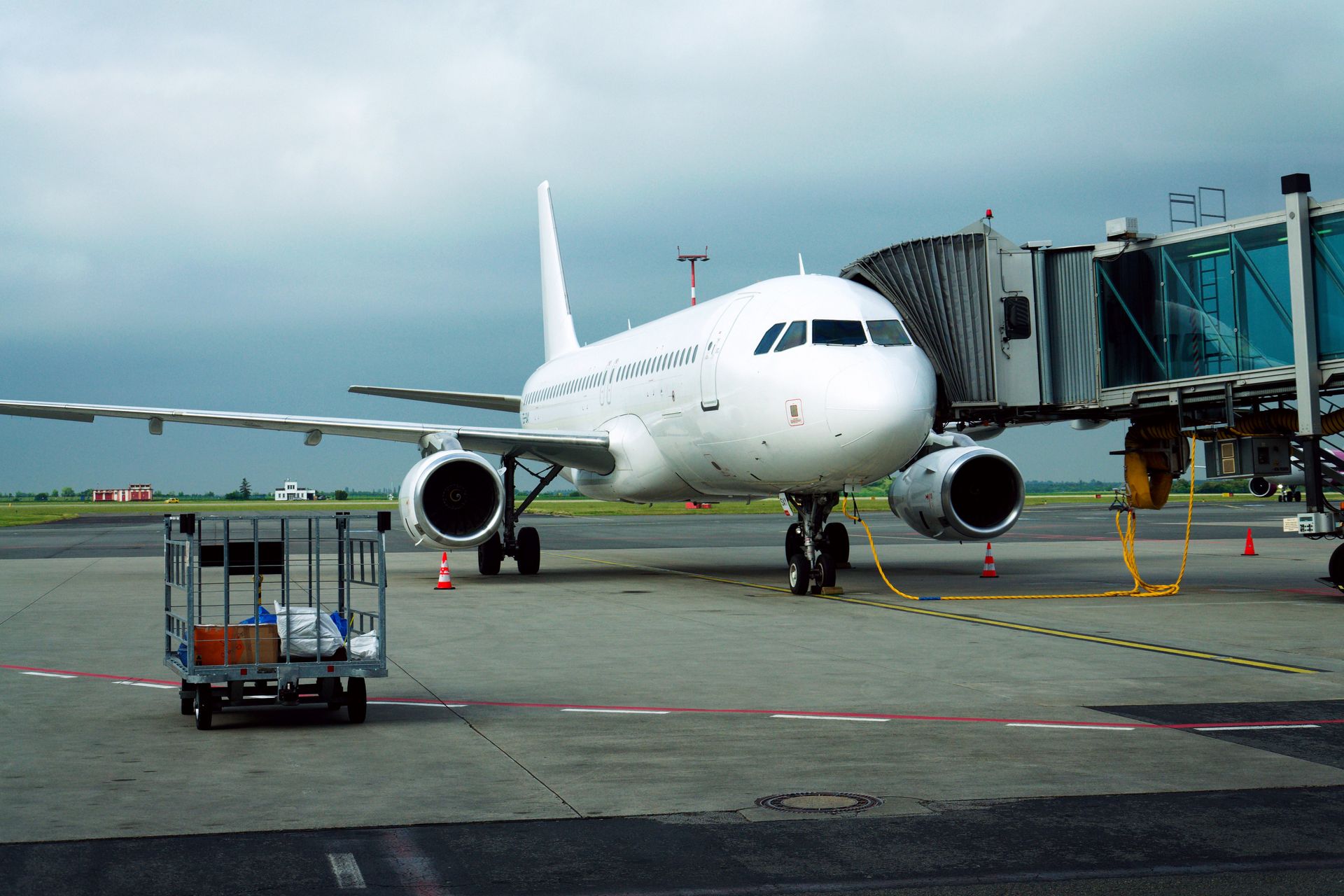 White passenger airplane parked on an airport tarmac beside a jet bridge under a cloudy sky