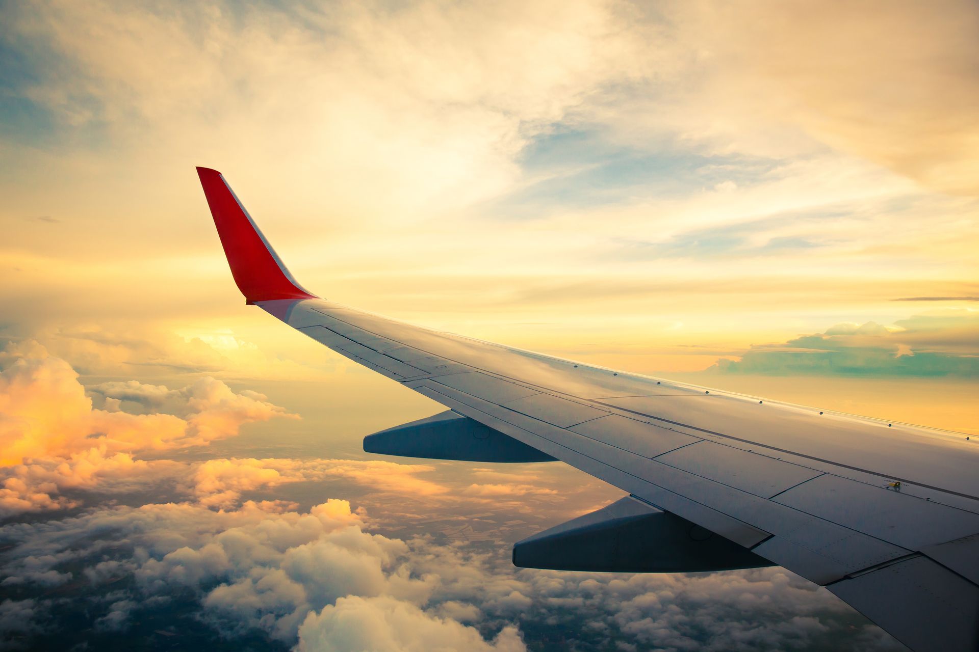 Airplane wing above clouds at sunset with a golden sky
