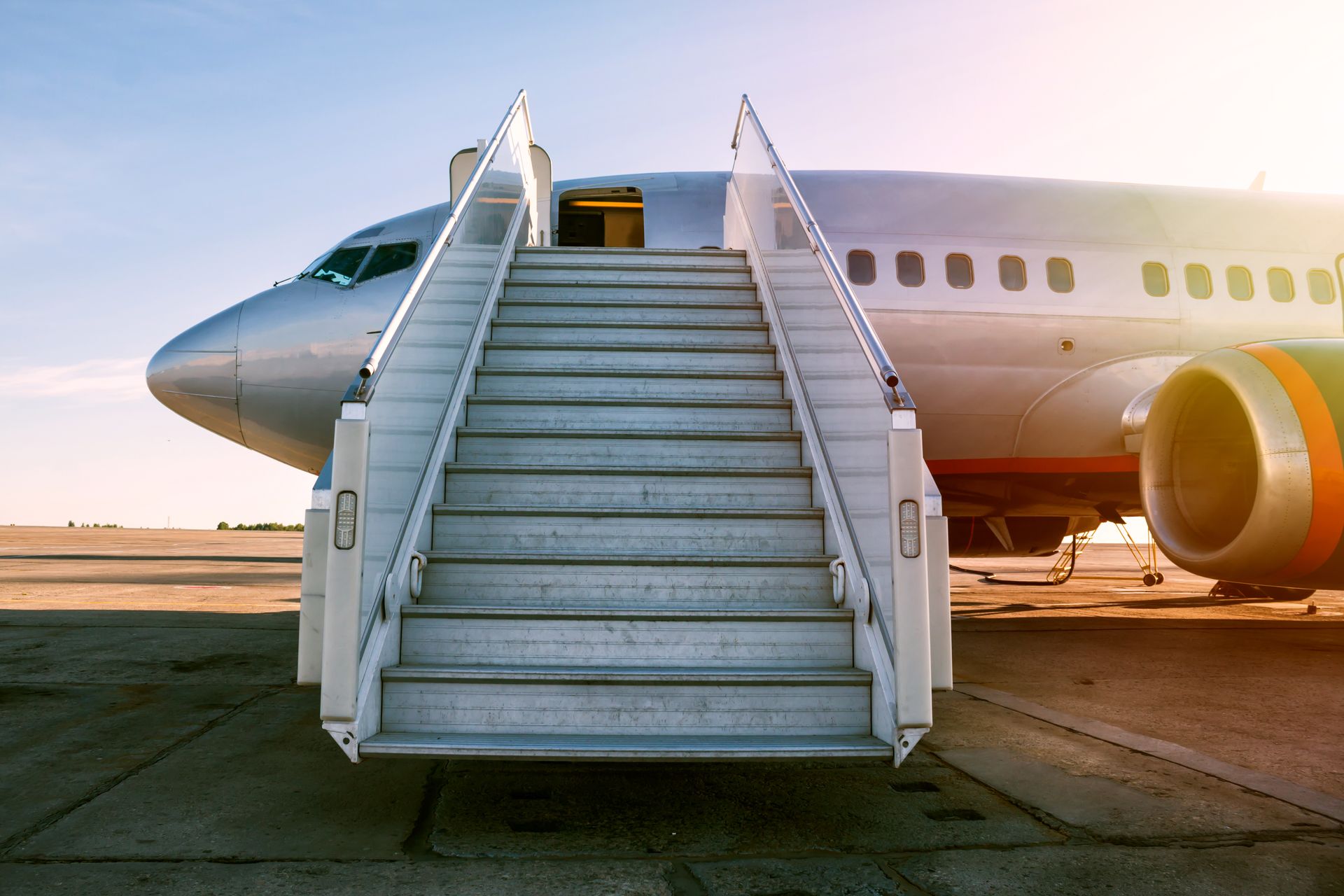Airplane boarding stairs at an airport, with a white jet on the tarmac at sunset