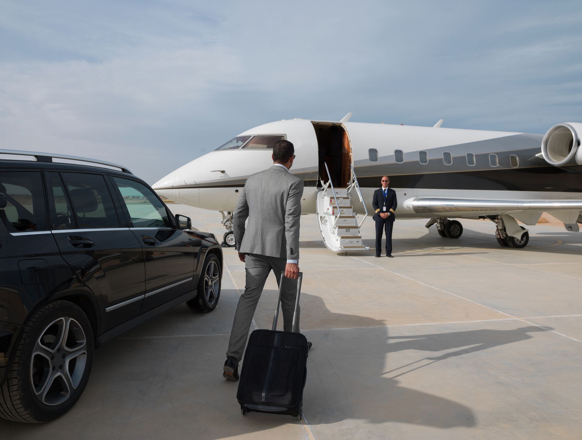 Person in a gray suit pulling luggage toward a private jet, with a black SUV nearby.