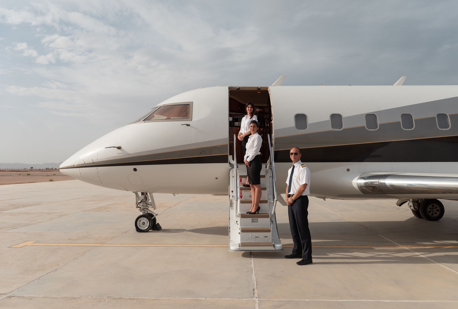 Private jet on tarmac with two people at the open stairs under a cloudy sky