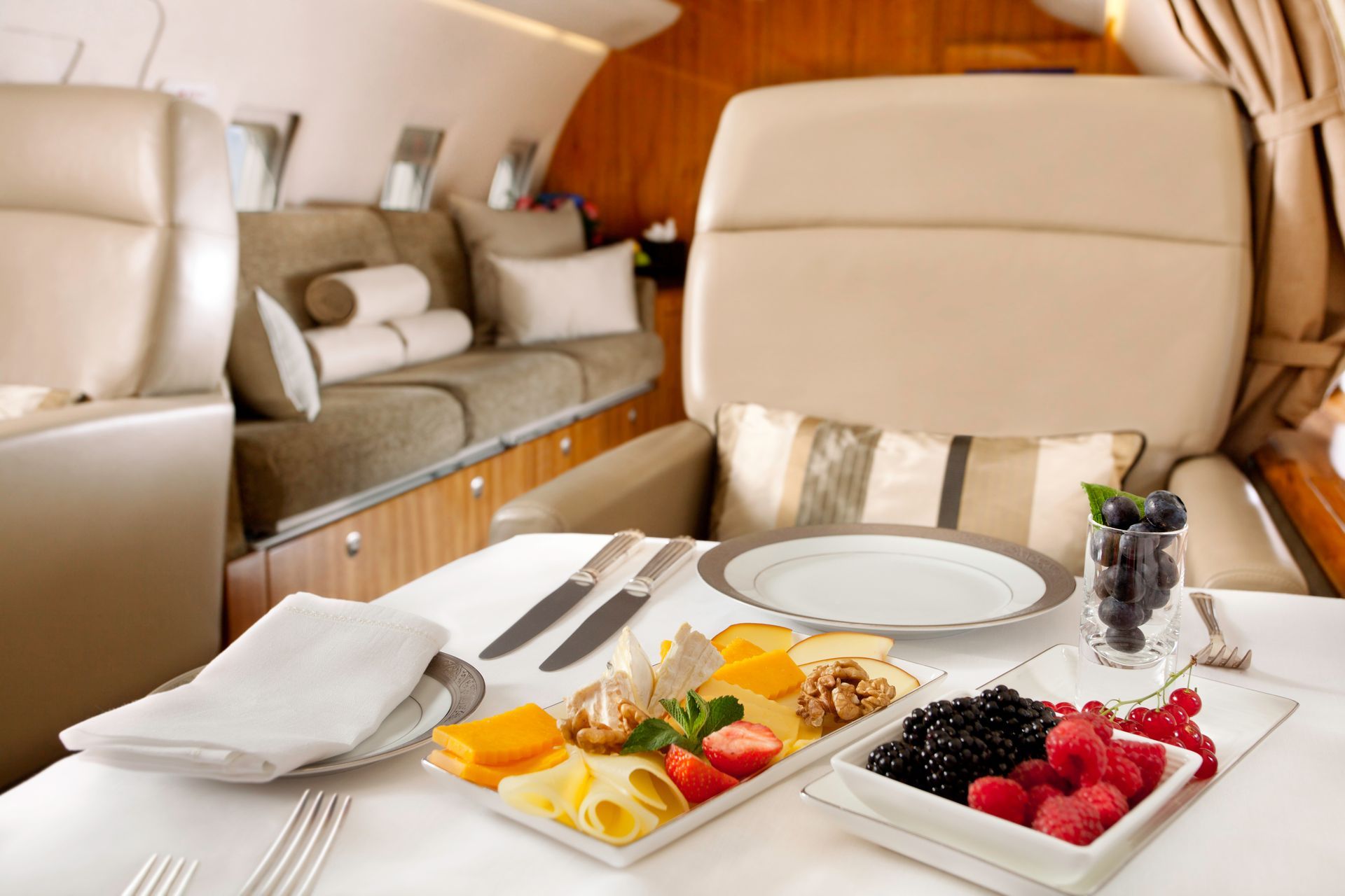 Luxury private jet cabin with set table of fruit, toast, utensils, and a glass of wine
