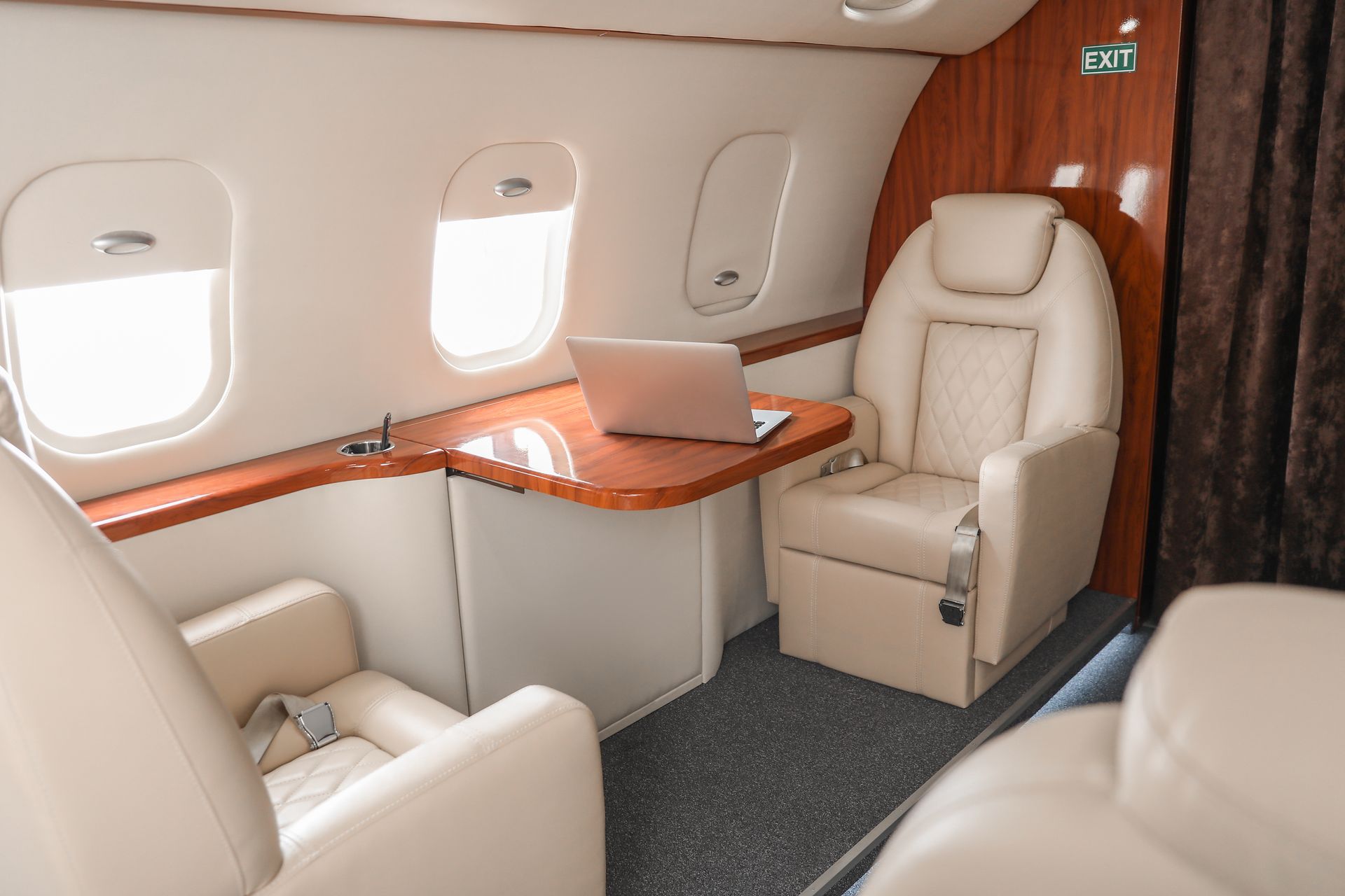 Luxury private jet cabin with cream seats, wood trim, and a laptop on the table by the windows