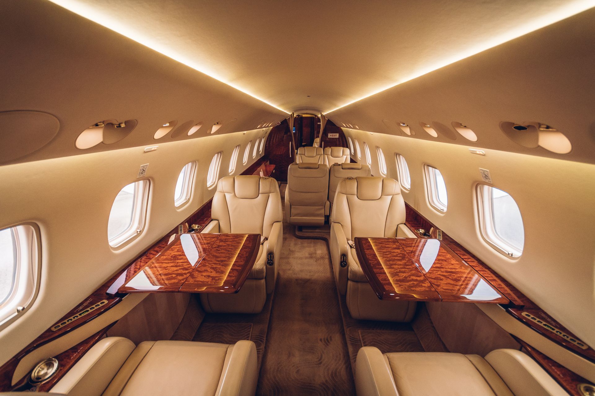 Luxury private jet cabin with beige leather seating and wood-trimmed tables, viewed down the aisle.