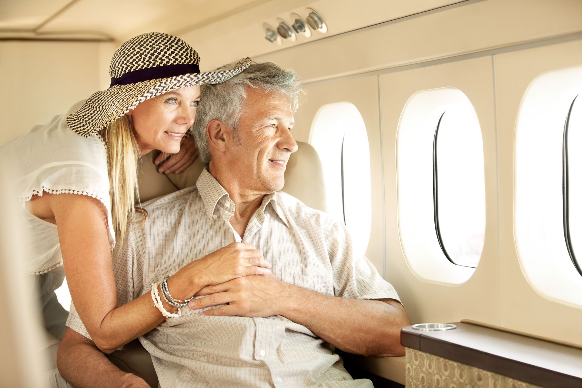 Couple sitting together on an airplane, smiling and looking out the window.