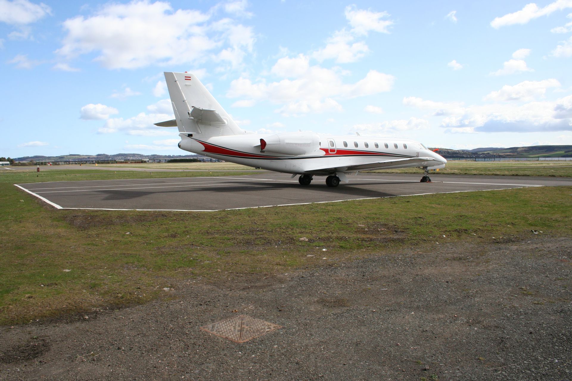 White private jet taxiing on a runway under a partly cloudy sky