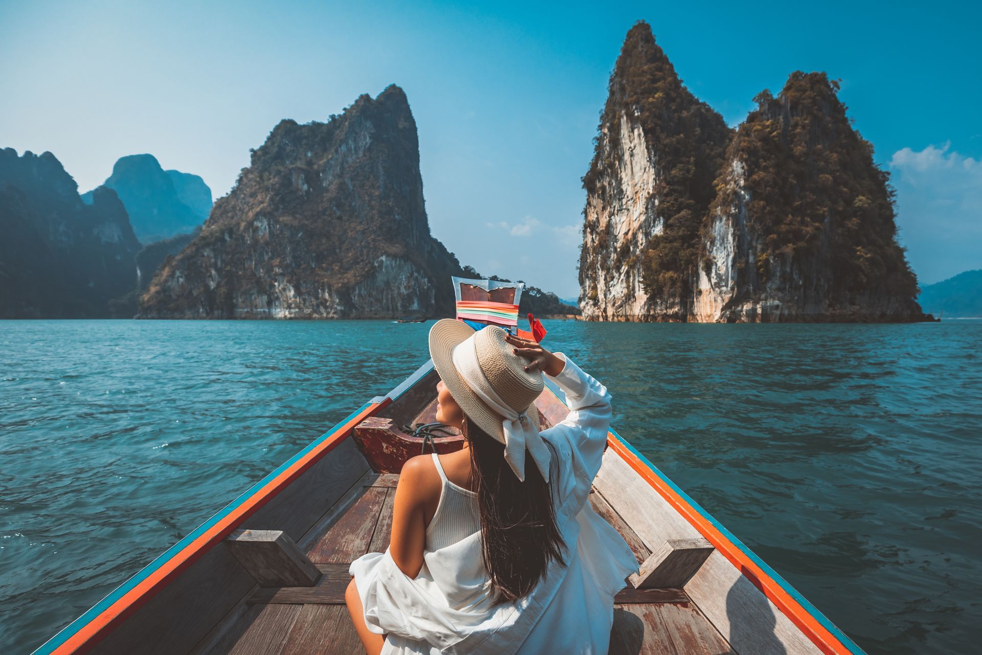 Person in a boat on turquoise water facing rocky island cliffs under a blue sky