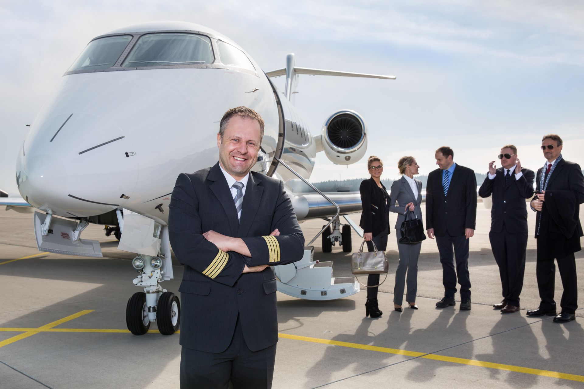 Man standing before a private jet on an airport tarmac, with a group of people in the background.