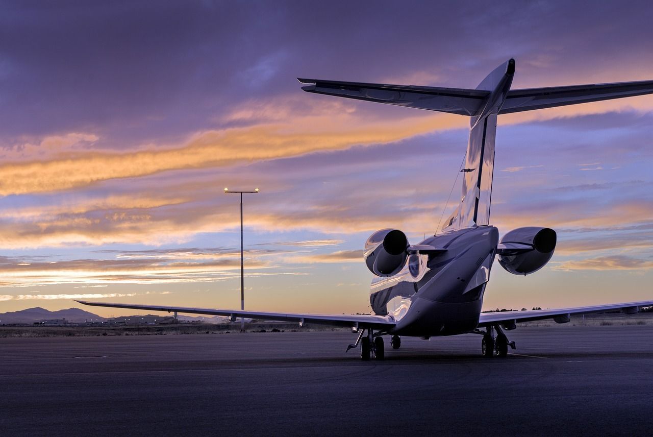 Private jet on airport tarmac at sunset, with colorful sky and distant runway lights