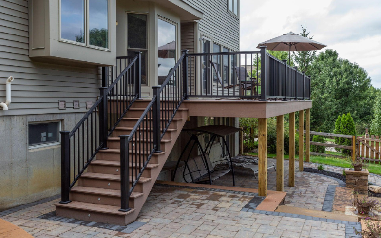 “Raised composite deck with stairs, black railing, and stone patio below built by deck builders in Allentown, PA”