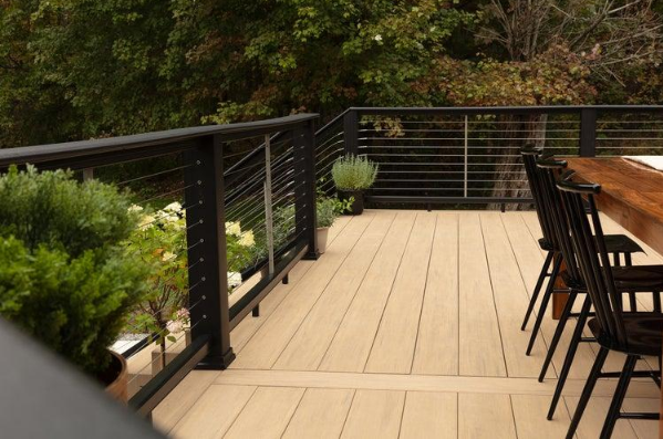 “Composite deck with black railing, outdoor dining chairs, and wooded backyard view by deck builders in Allentown, PA”