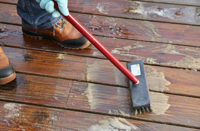 “Worker coating weathered deck boards with a roller to refresh the surface during repair by deck builders in Allentown, PA”