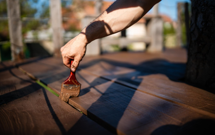 “Hand applying stain to dark wood deck boards with a brush during repair work by deck builders in Allentown, PA”