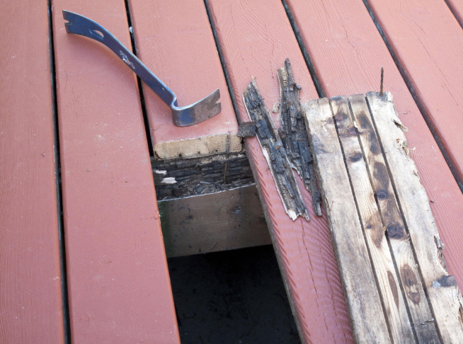 “Damaged red deck boards being lifted with a pry bar to expose worn framing during repair by deck builders in Allentown, PA”