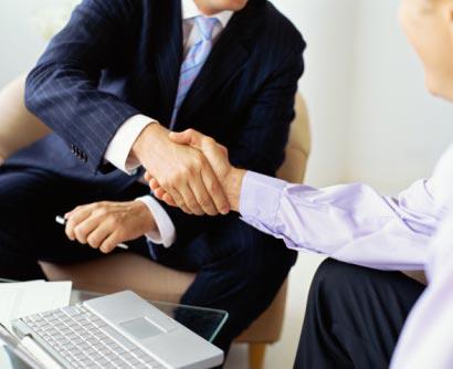 Two men shaking hands in front of a laptop