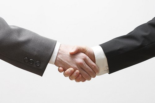Two men in suits are shaking hands on a white background.