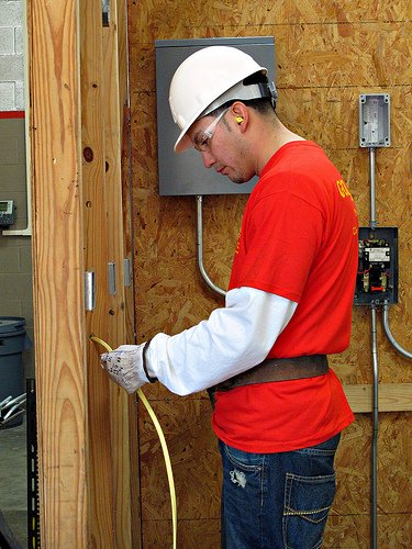A man wearing a hard hat and a red shirt is working on electrical wires