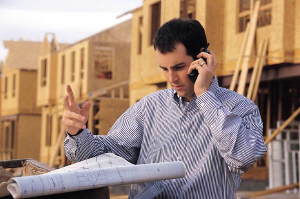 A man is talking on a cell phone while looking at blueprints