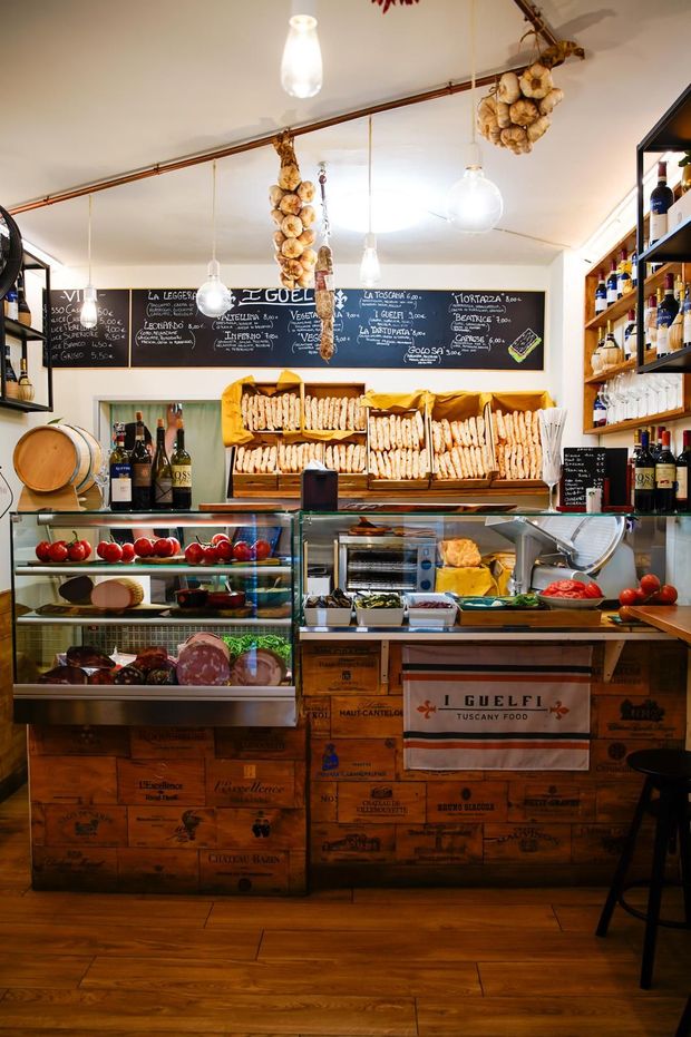 Accogliente bancone di panetteria con pasticcini, pane, menù su lavagna e vetrine in legno in un negozio illuminato da una luce calda.