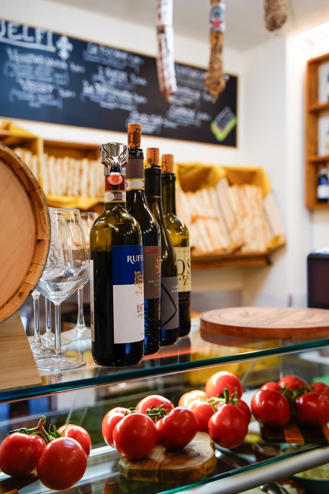 Bottiglie di vino e pomodori su un bancone di vetro in un mercato o negozio rustico.