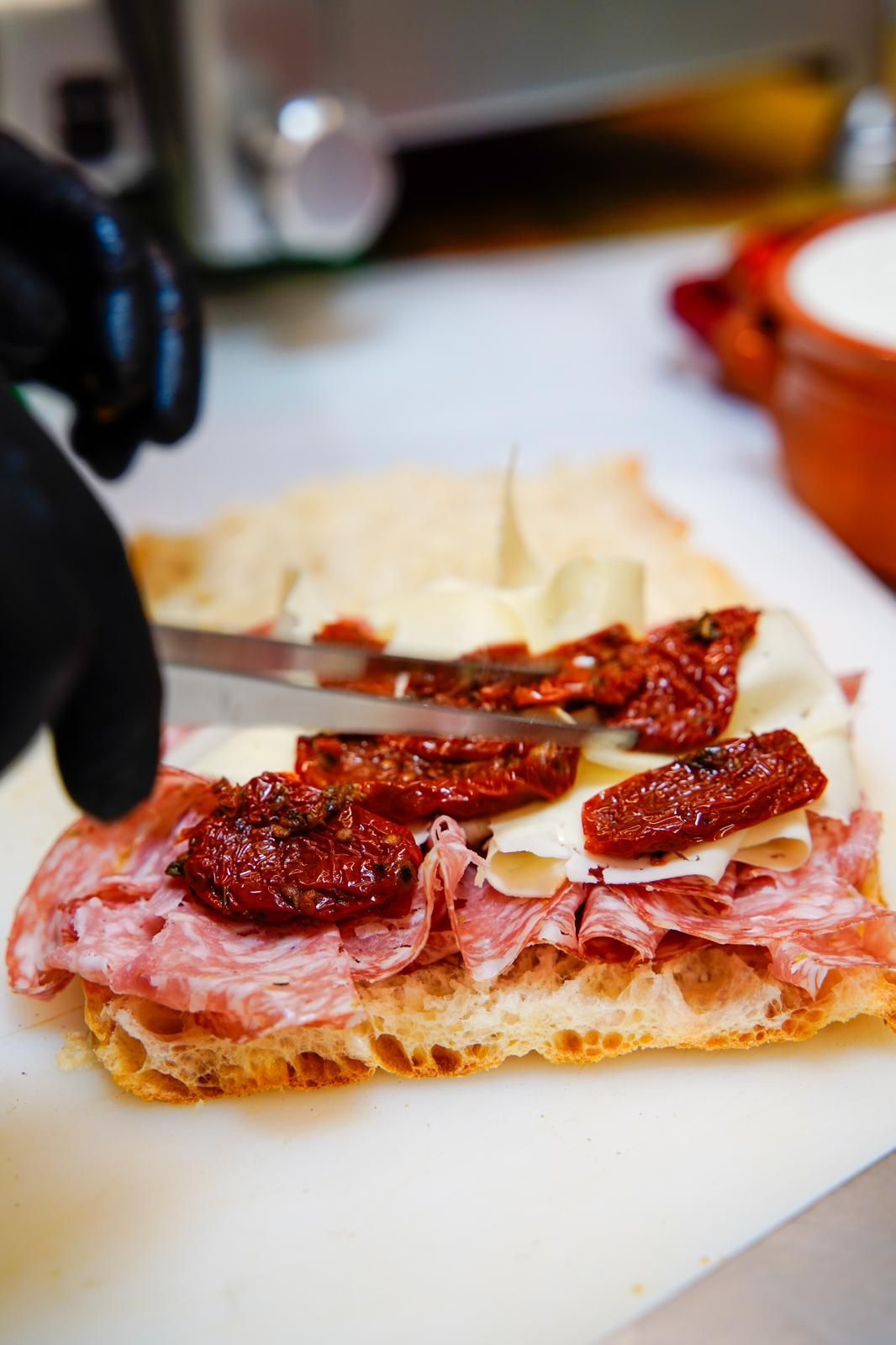 Sandwich aperto con affettati e pomodori secchi su pane, su un tagliere
