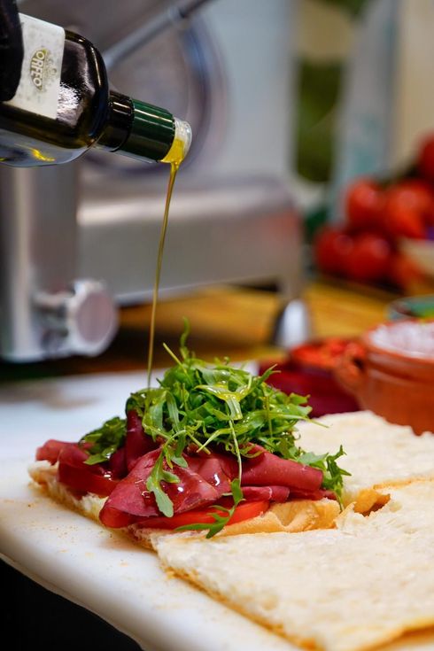 Olio d'oliva che cola su una focaccia in stile caprese con pomodori e verdure in una cucina