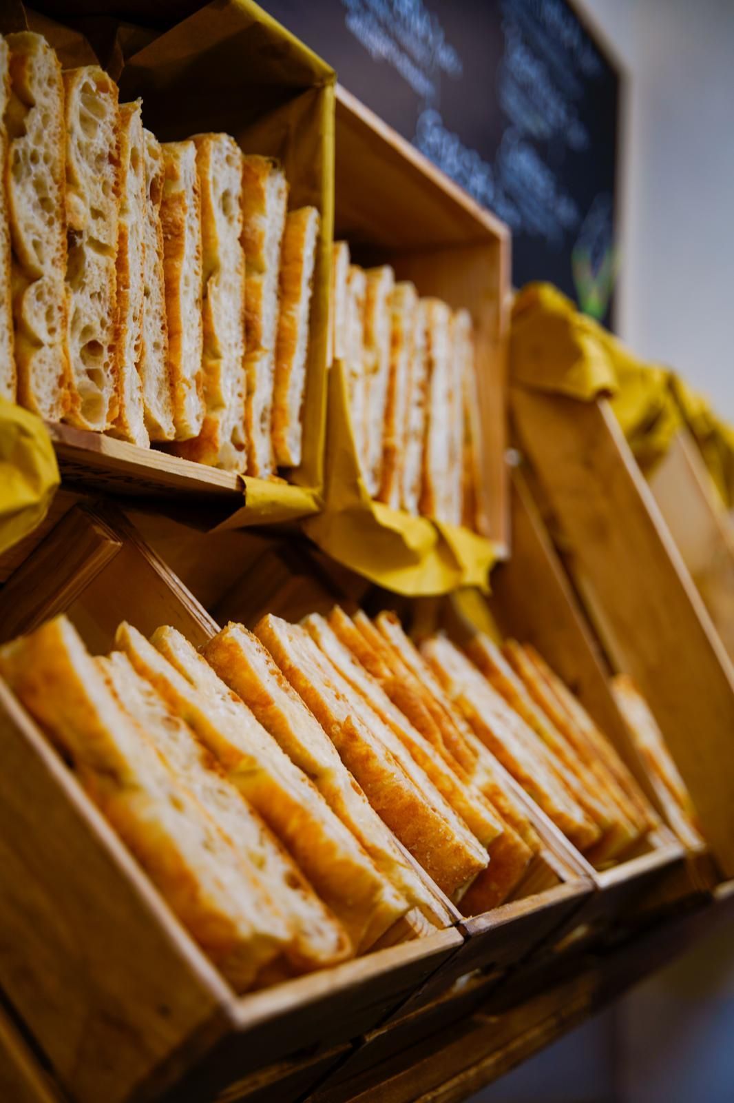 Espositore da mercato in legno con spicchi di formaggio o pasticcini ordinatamente impilati su scaffali, con una lavagna sullo sfondo.