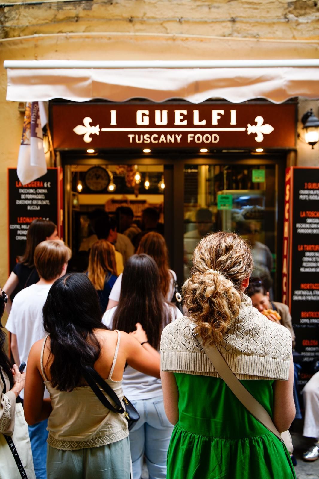 Di sera, una folla si è radunata fuori dal ristorante Gulefi Tuscan Food, di fronte all'ingresso illuminato.