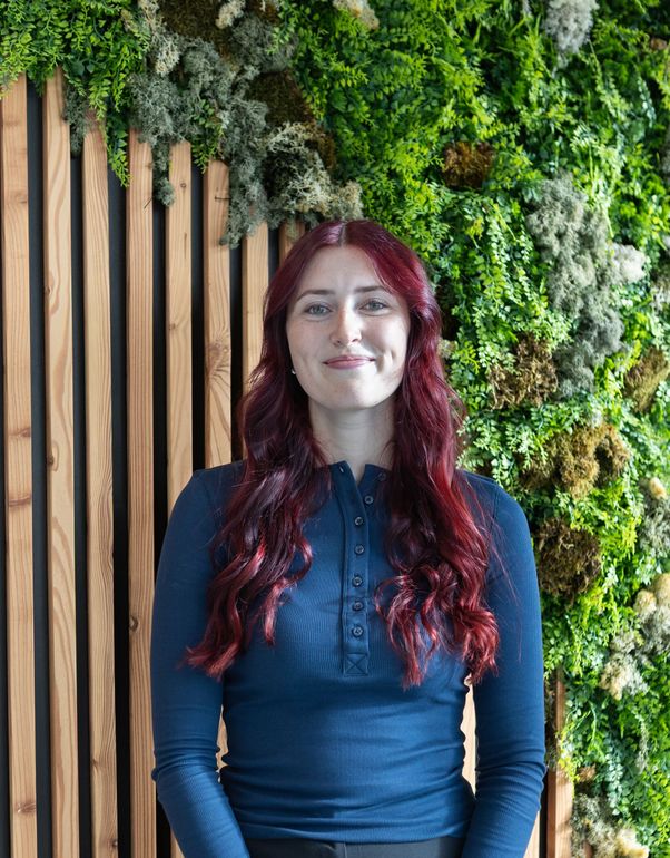 Smiling woman with long hair and folded arms, wearing a light lavender blouse against a white background