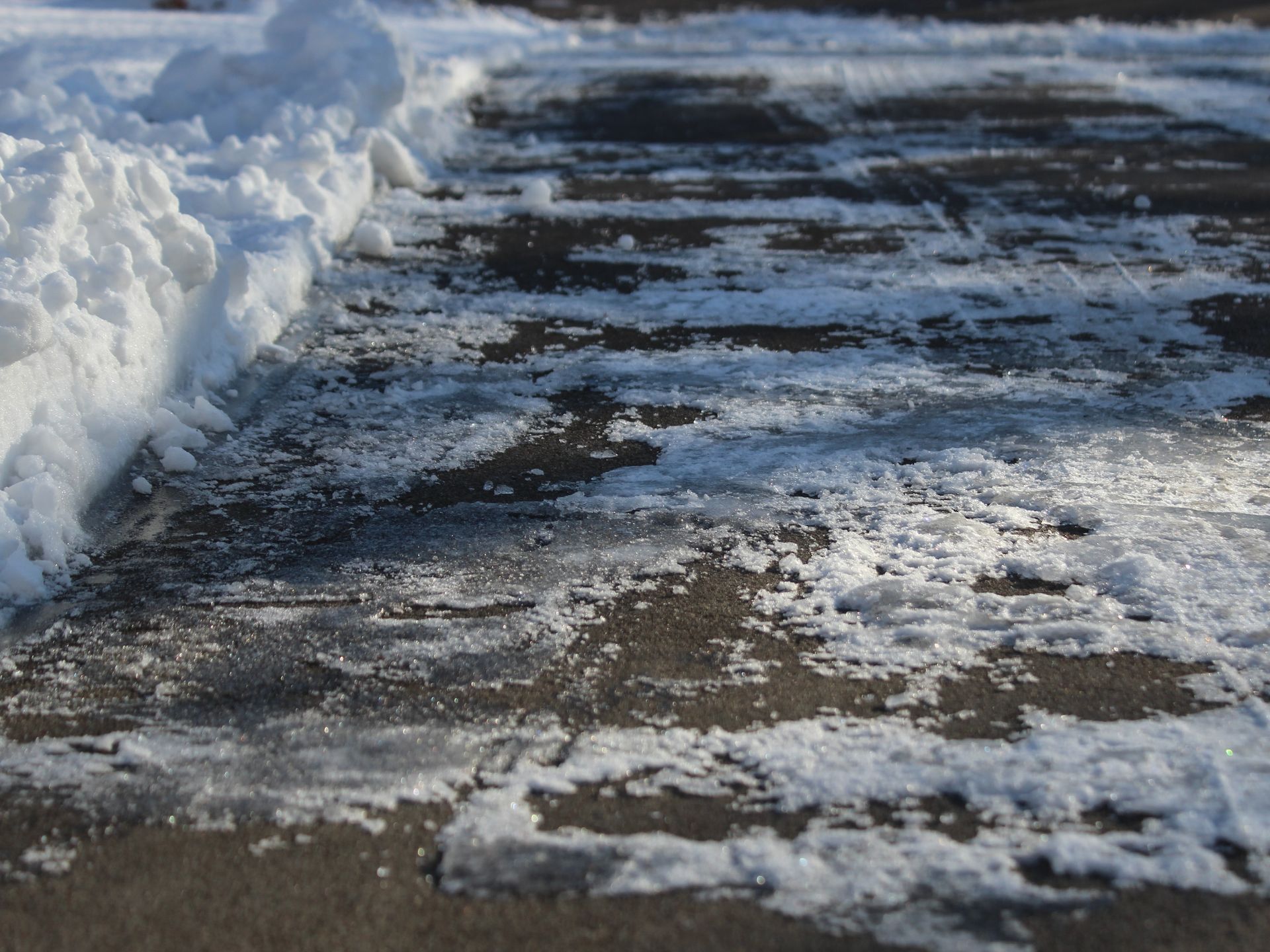 Snow and ice on a dark pavement, partially cleared.