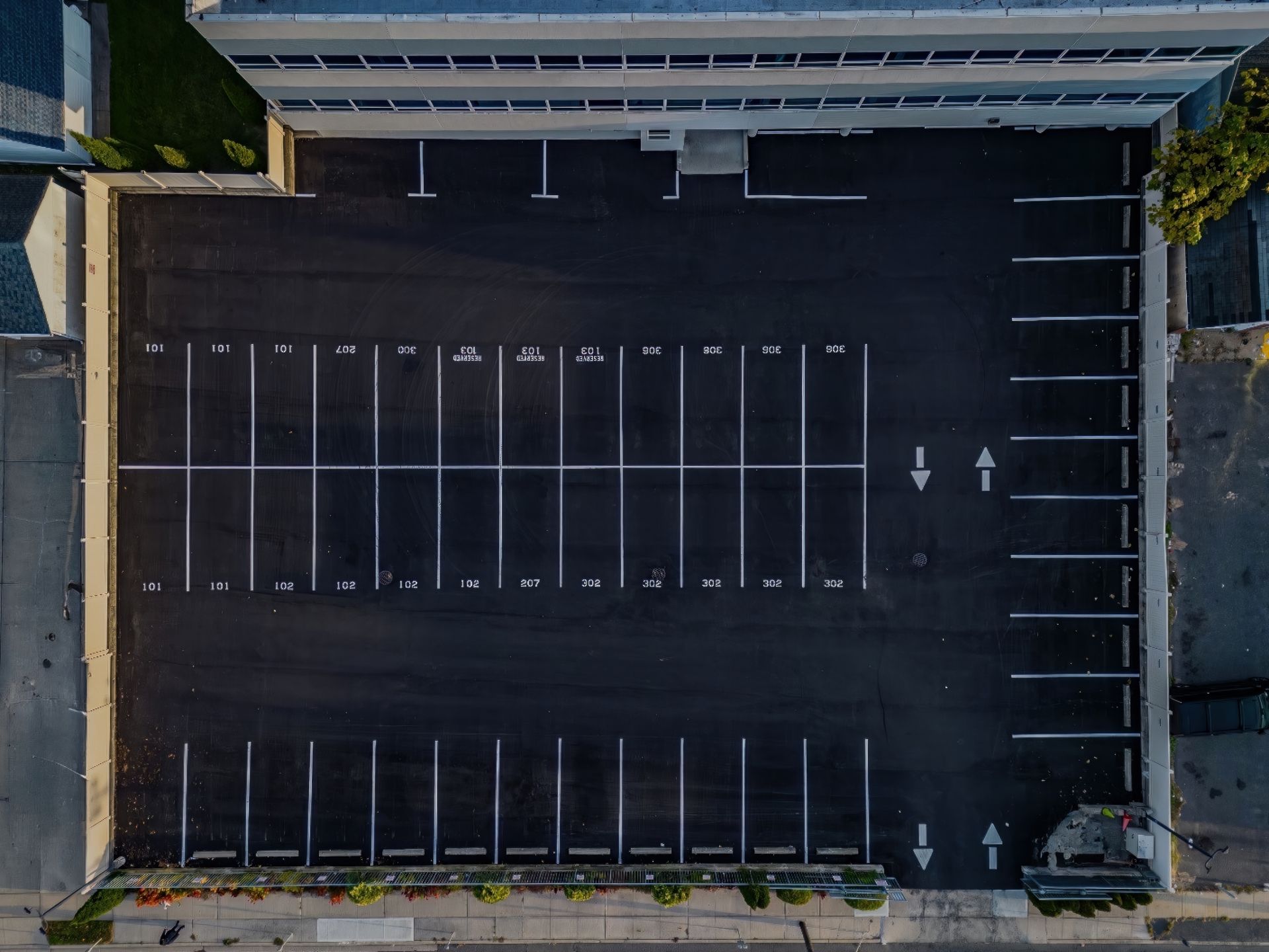 Empty parking lot beside a building, with painted spaces and a few trees along the edges