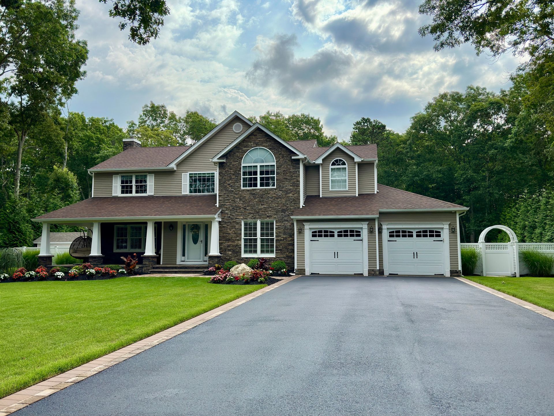 Two-story suburban house with a large driveway, two-car garage, and manicured lawn under a cloudy sky
