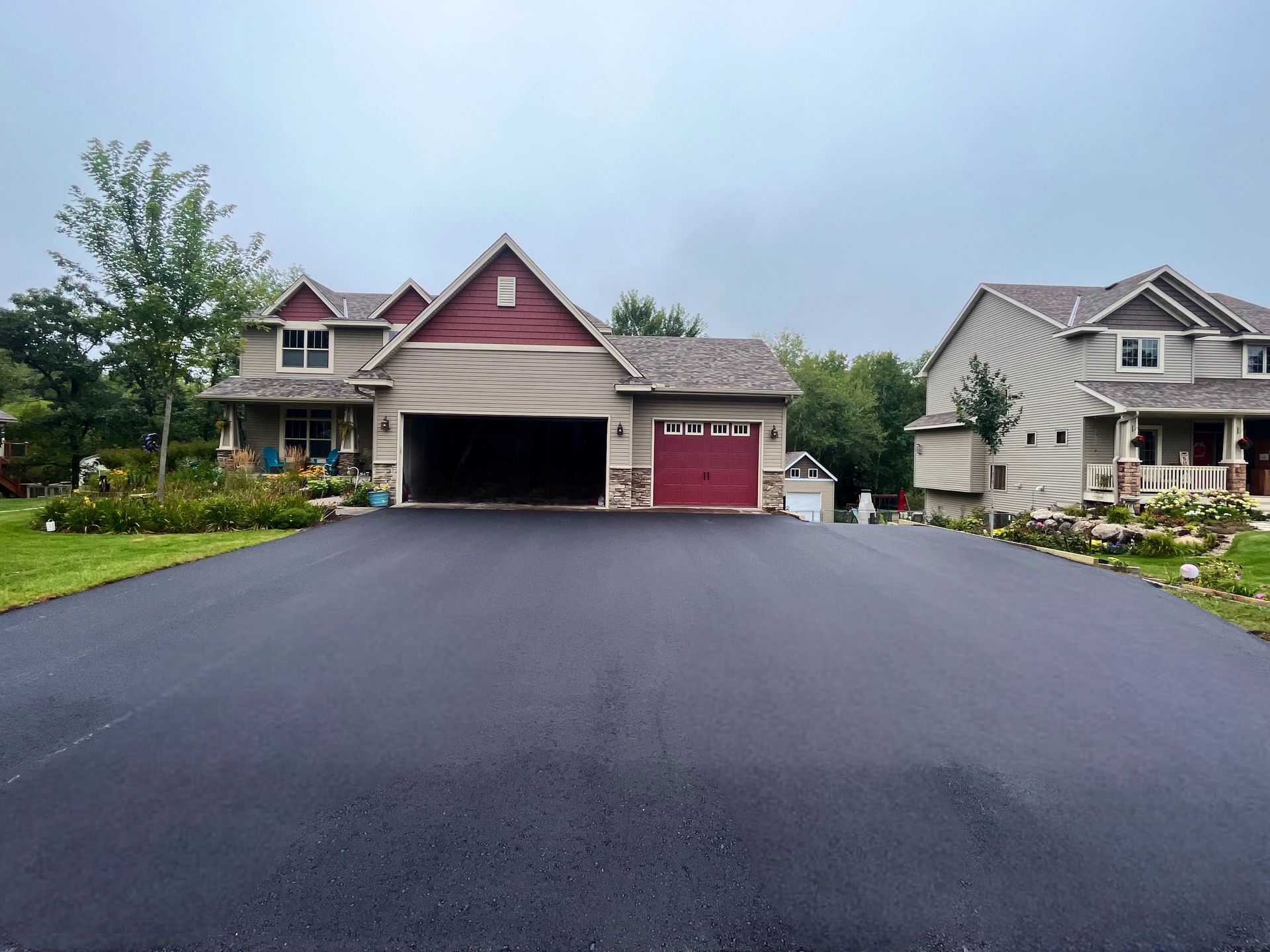 Newly paved asphalt driveway leading to a multi-car garage on a house with red accents.
