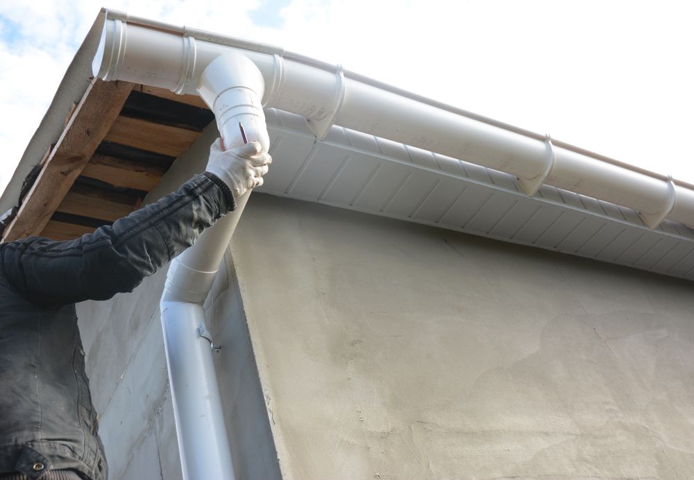 A Man is Installing a White Gutter on the Side of a House A Roof — Nathan Parnell Roofing In Nowra, NSW