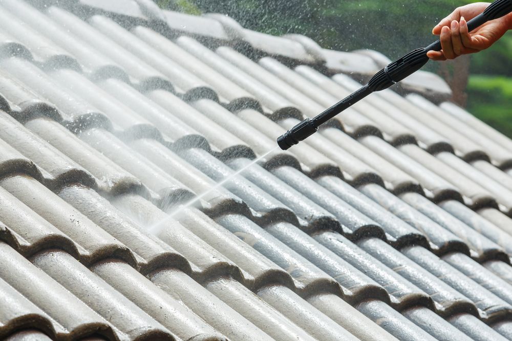 A Person is Cleaning a Tiled Roof With a High Pressure Washer — Nathan Parnell Roofing In Ulladulla, NSW