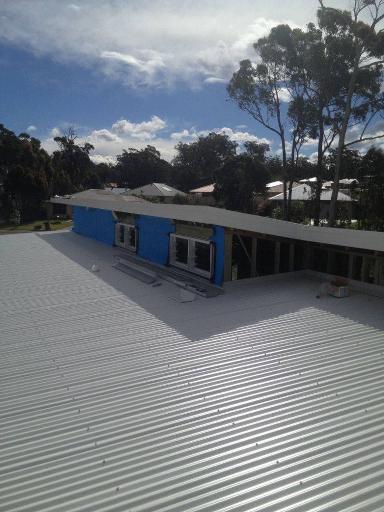 A White Roof With a Blue Building in the Background  — Nathan Parnell Roofing In Culburra, NSW