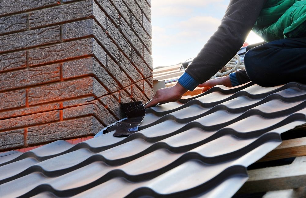 A Man is Working on a Roof With a Brick Chimney in the Background — Nathan Parnell Roofing In Sussex Inlet, NSW