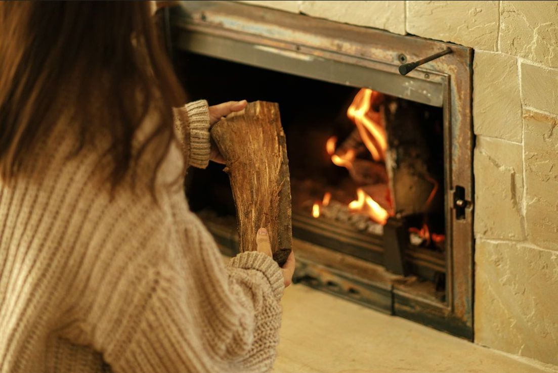 A Woman is Holding a Log in Front of a Fireplace — Nathan Parnell Roofing In Culburra, NSW
