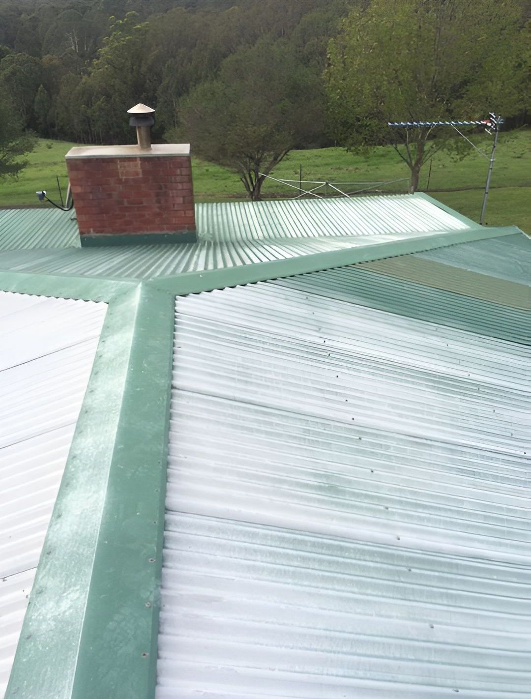 A Roof With a Chimney on Top of It and Trees in the Background  — Nathan Parnell Roofing In Nowra, NSW
