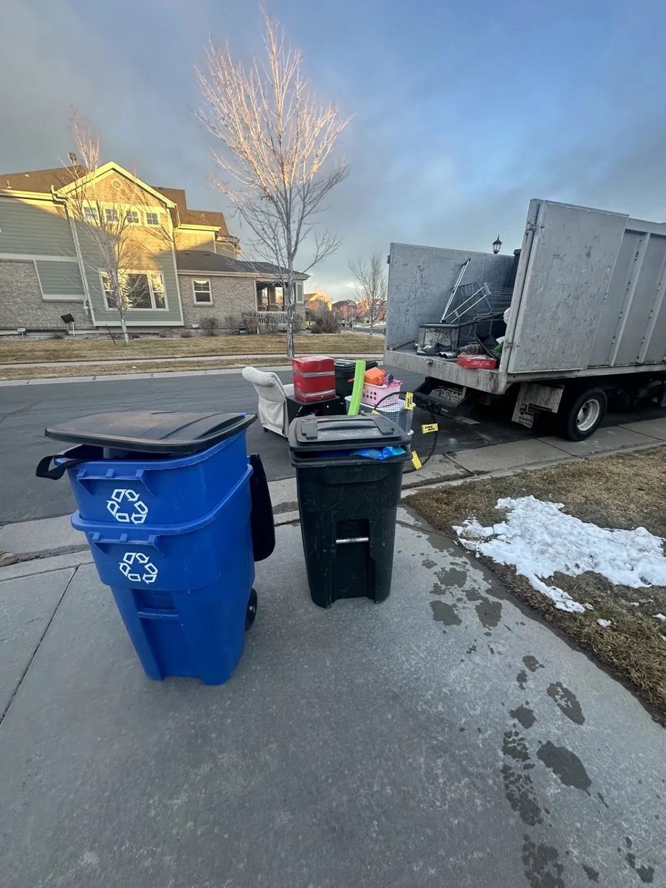 Two trash cans are sitting on the sidewalk next to a garbage truck.