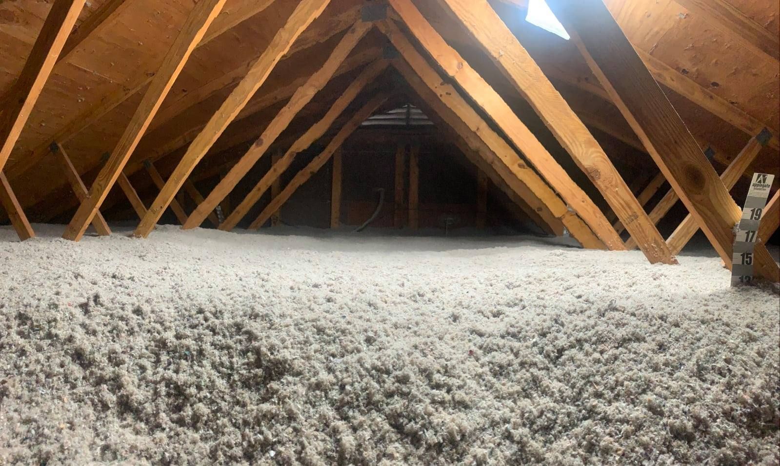 Attic space filled with gray insulation between wooden beams.