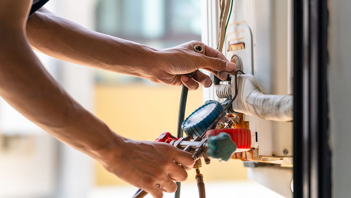 Hands of a technician attaching gauges to an air conditioning unit.