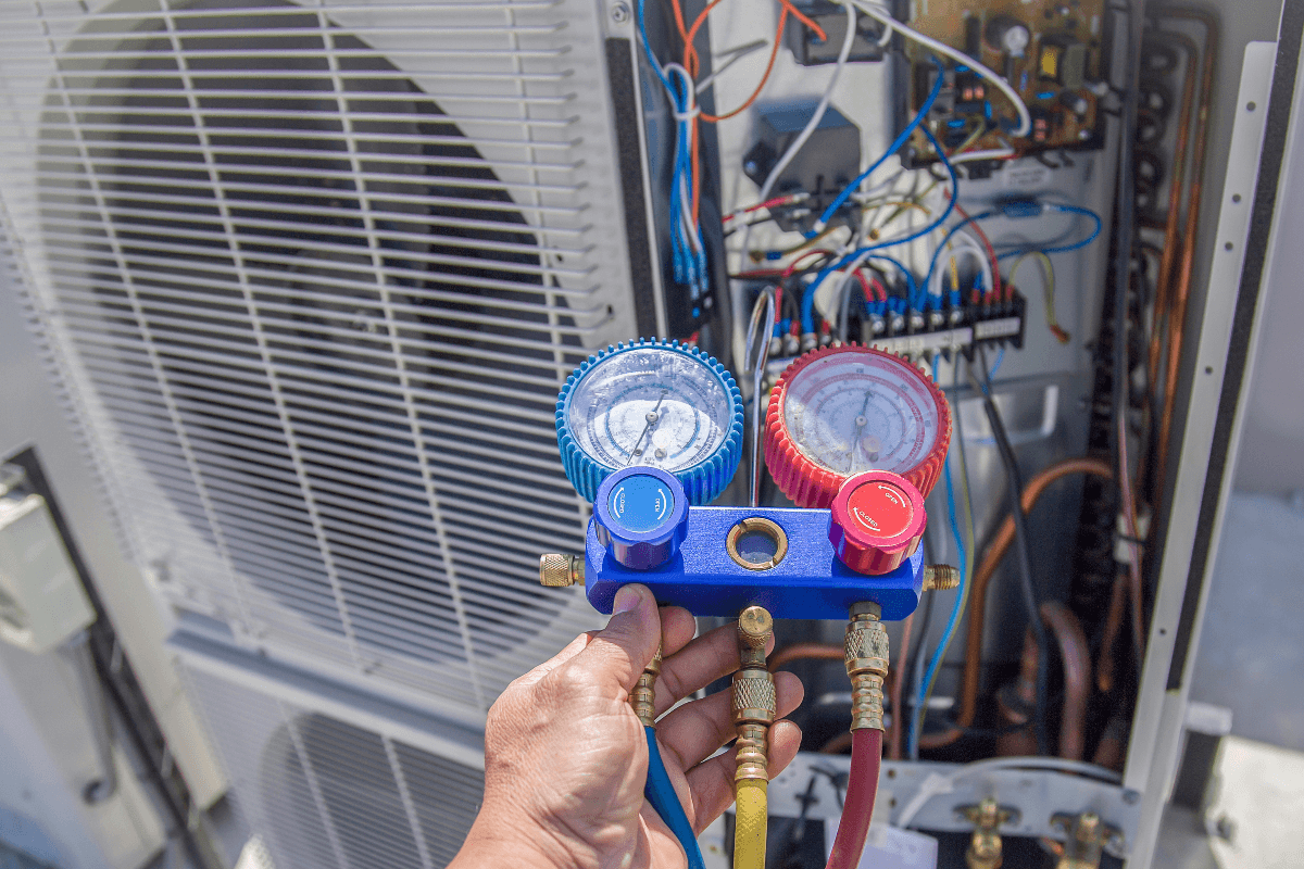 AC unit being serviced. Technician uses gauges to check refrigerant pressure.